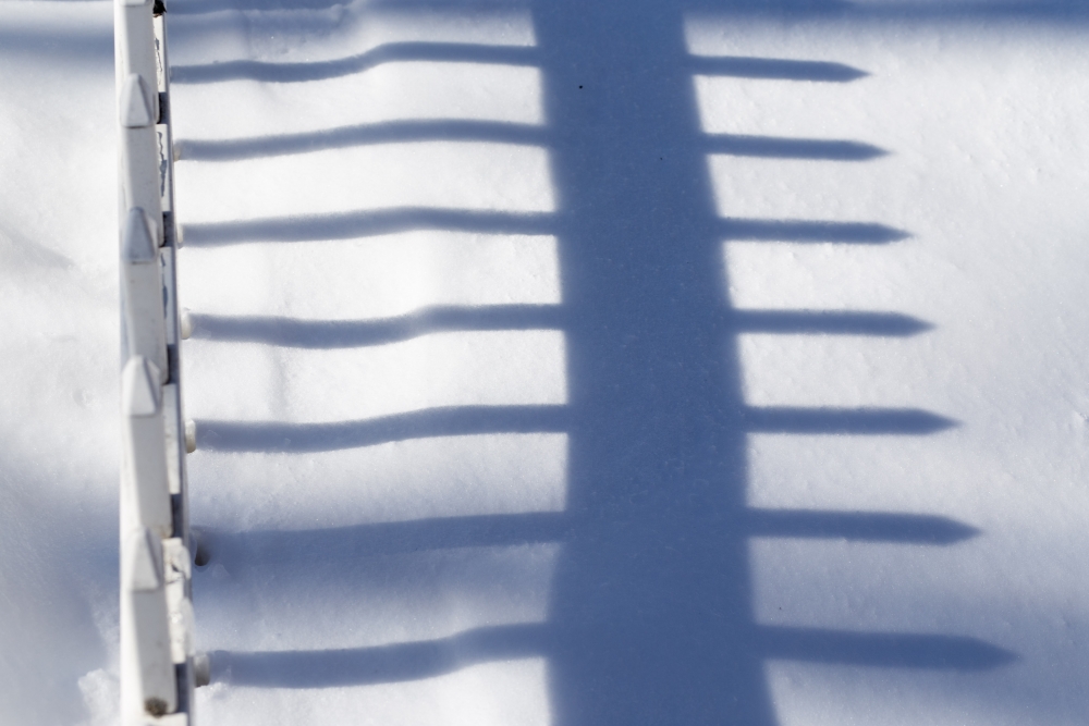 Shadows | Nearly covered by the snow, a pickett fence casts a long shadow in the afternoon light. (Herald / Tim Calabro)